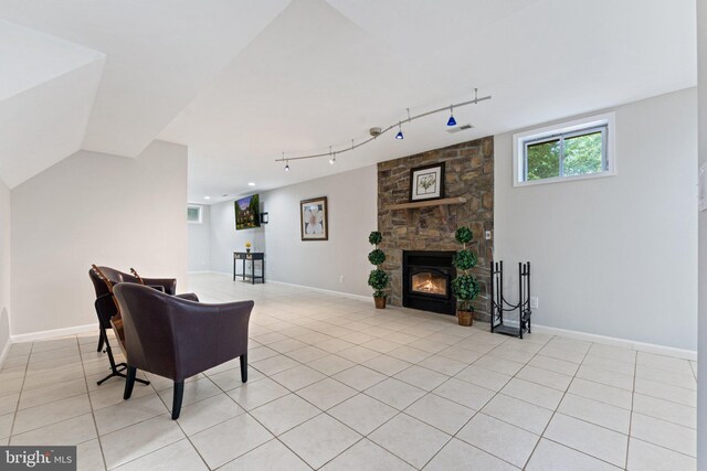 living room featuring light tile patterned flooring, rail lighting, a stone fireplace, and baseboards