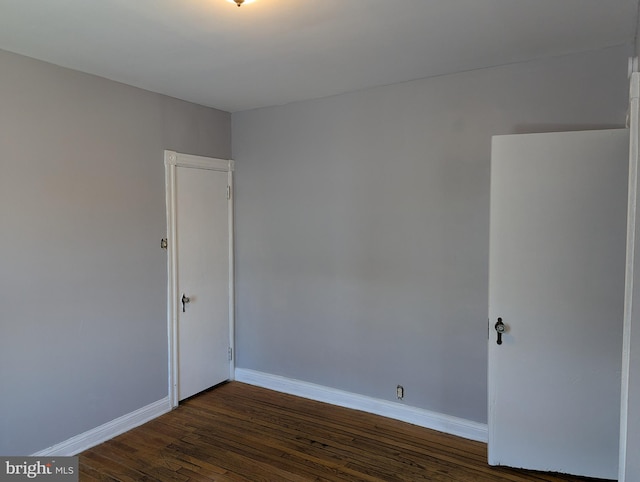 spare room with baseboards and dark wood-style flooring