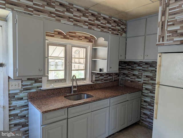 kitchen featuring freestanding refrigerator, a sink, open shelves, tasteful backsplash, and dark stone counters