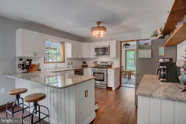 kitchen with stainless steel appliances, a peninsula, dark wood finished floors, white cabinets, and decorative backsplash