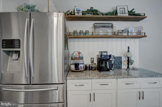 kitchen with stainless steel fridge, open shelves, and white cabinetry