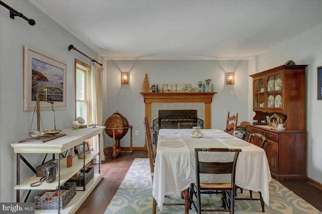 dining room with dark wood-style floors, a tiled fireplace, and baseboards