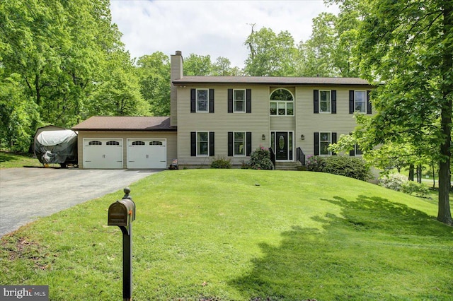 colonial-style house featuring driveway, a garage, a chimney, and a front lawn
