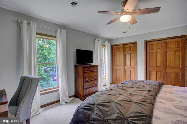 bedroom with light colored carpet, baseboards, two closets, and a ceiling fan