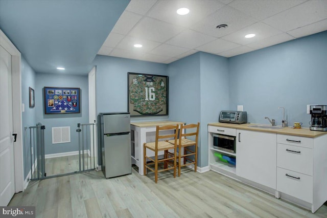 bar featuring stainless steel appliances, a sink, light wood finished floors, baseboards, and a drop ceiling