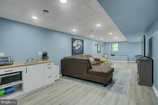 living area featuring light wood-type flooring, baseboards, a paneled ceiling, and recessed lighting