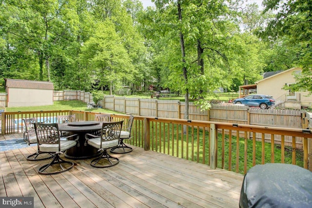 deck featuring outdoor dining space, an outbuilding, a shed, and view of scattered trees