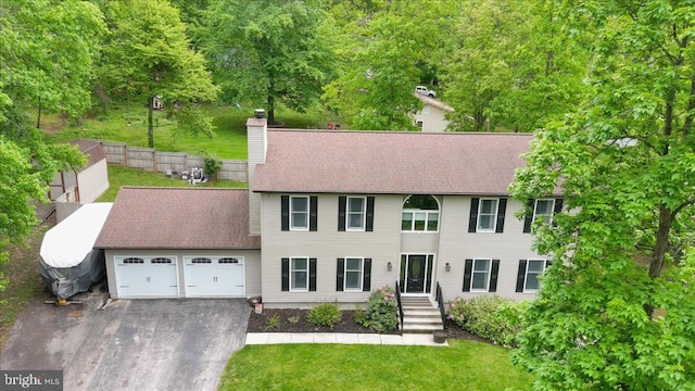 colonial home with asphalt driveway, a garage, a chimney, and a shingled roof