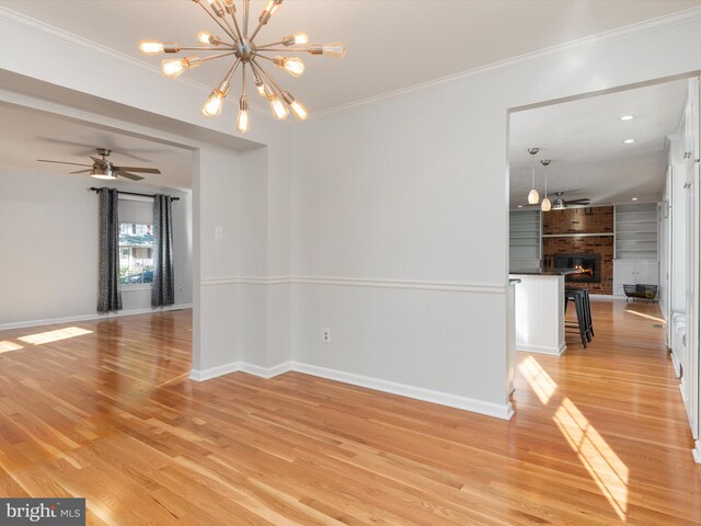 empty room featuring light wood-style flooring, baseboards, ornamental molding, a chandelier, and a fireplace