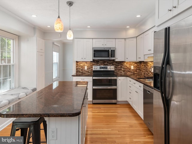 kitchen with appliances with stainless steel finishes, light wood finished floors, white cabinetry, ornamental molding, and decorative backsplash