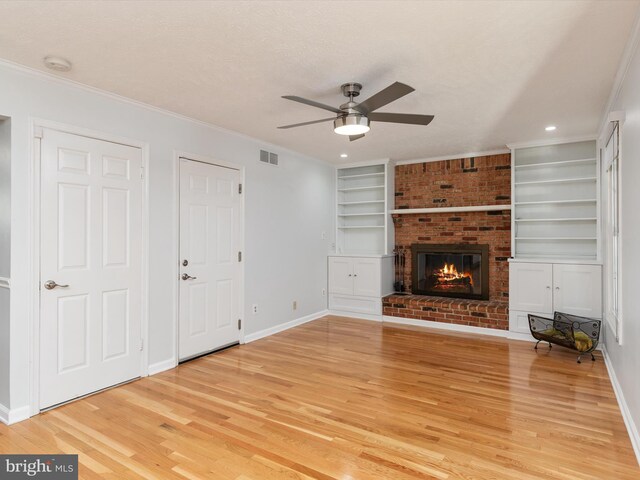 unfurnished living room featuring built in shelves, a ceiling fan, light wood finished floors, a fireplace, and ornamental molding