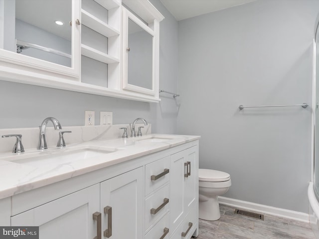full bath with toilet, wood finished floors, double vanity, and baseboards