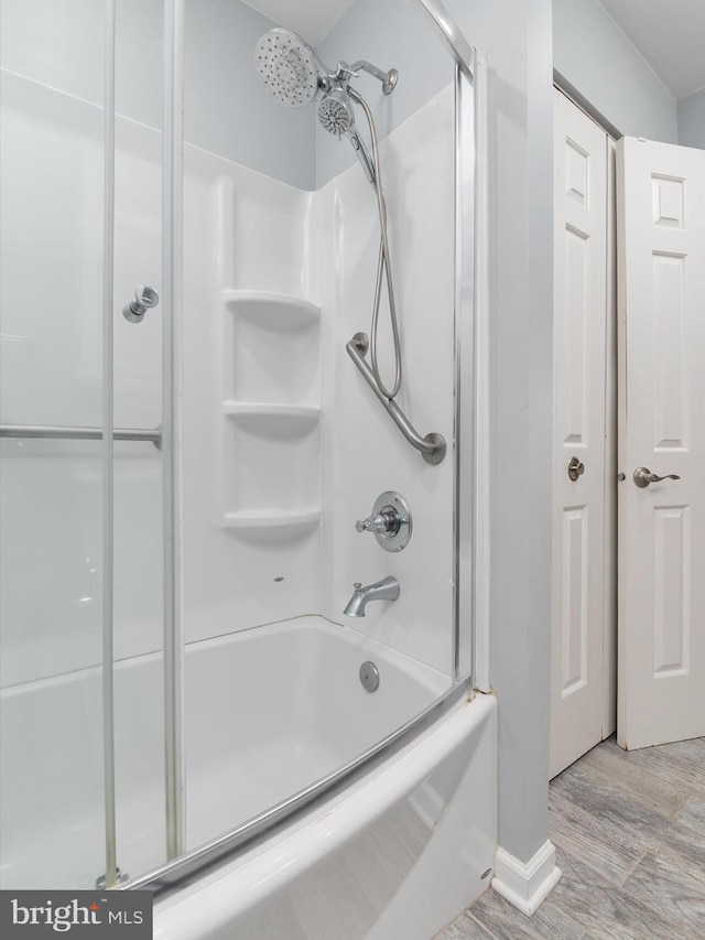 bathroom featuring wood finished floors, enclosed tub / shower combo, and baseboards