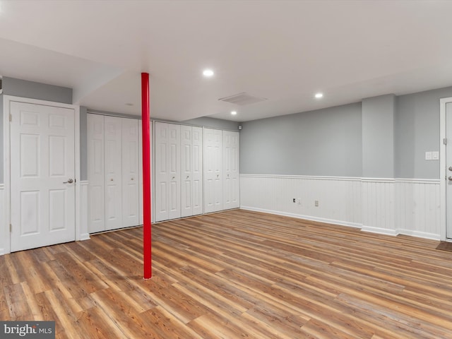 finished below grade area featuring wood finished floors, a wainscoted wall, and recessed lighting
