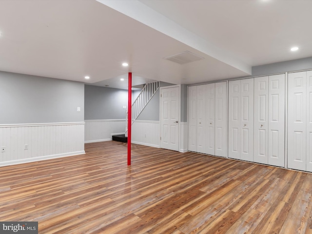 finished below grade area with light wood-style floors, a wainscoted wall, and recessed lighting