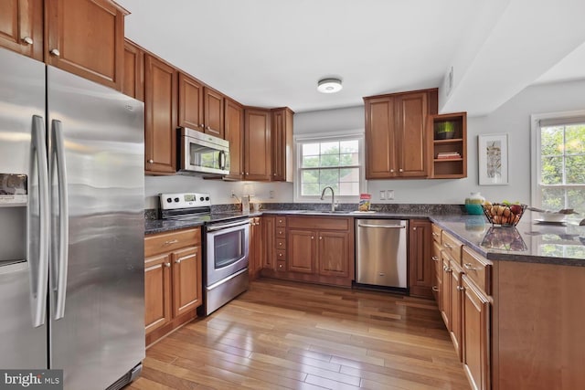 kitchen featuring stainless steel appliances, brown cabinetry, a sink, open shelves, and hardwood / wood-style floors