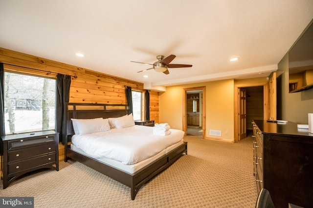 bedroom with recessed lighting, light colored carpet, ensuite bath, wood walls, and a ceiling fan