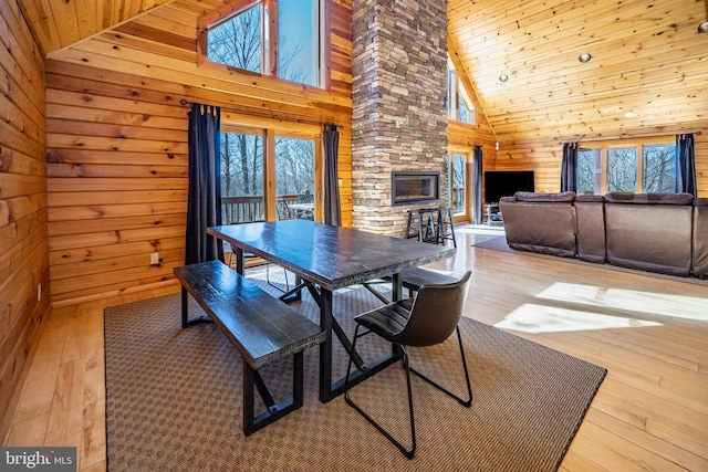 dining room featuring wood walls, high vaulted ceiling, wood-type flooring, a fireplace, and wood ceiling