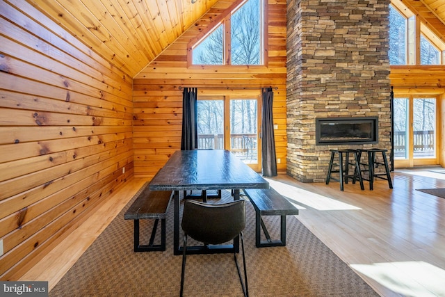 dining space with wood finished floors, wooden walls, wood ceiling, a fireplace, and high vaulted ceiling