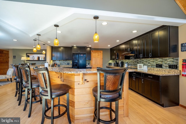 kitchen with black fridge, tasteful backsplash, light wood finished floors, a kitchen breakfast bar, and recessed lighting