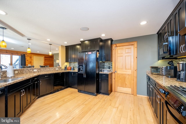 kitchen featuring black appliances, a sink, decorative light fixtures, light stone counters, and recessed lighting