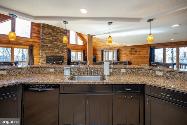 kitchen featuring black dishwasher, a sink, wood walls, decorative light fixtures, and stone counters