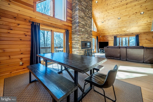 dining room featuring high vaulted ceiling, a fireplace, wooden walls, and wood finished floors