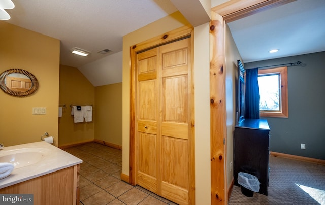 bathroom featuring lofted ceiling, vanity, baseboards, and tile patterned flooring