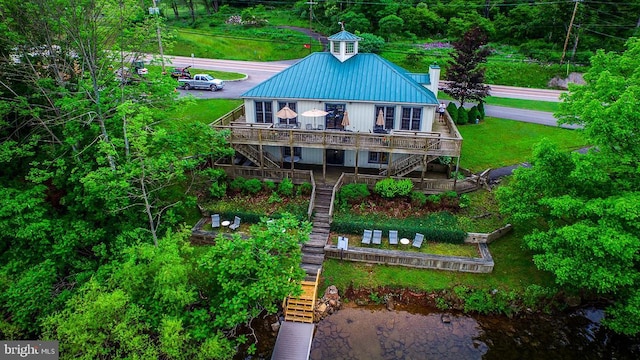 back of property with stairway, a chimney, metal roof, a deck with water view, and a lawn