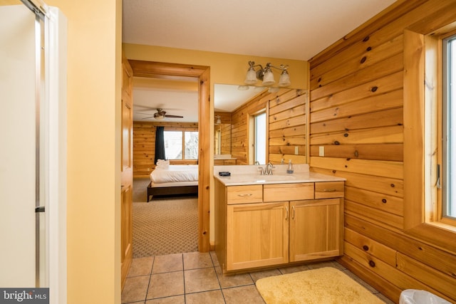 full bath with ensuite bathroom, wooden walls, vanity, tile patterned floors, and a ceiling fan