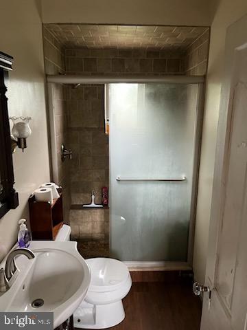 full bath featuring a sink, a stall shower, wood finished floors, and toilet