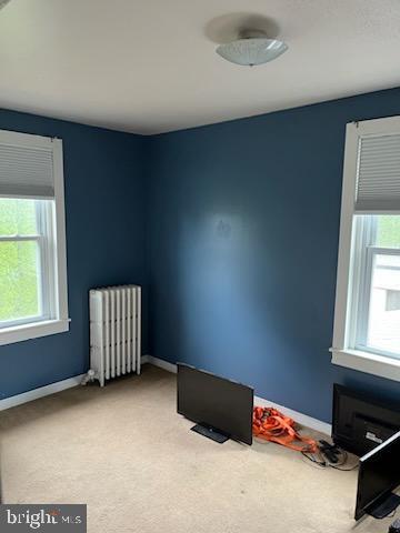 spare room with radiator heating unit, light colored carpet, and healthy amount of natural light