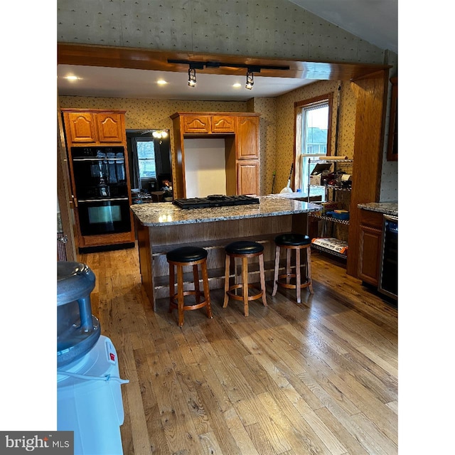 kitchen featuring black appliances, wallpapered walls, wine cooler, light wood-style flooring, and a kitchen island