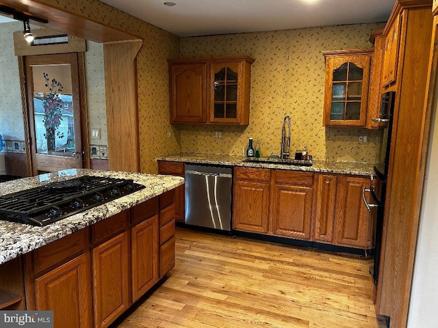 kitchen featuring black gas stovetop, dishwasher, a sink, wallpapered walls, and light wood-style floors