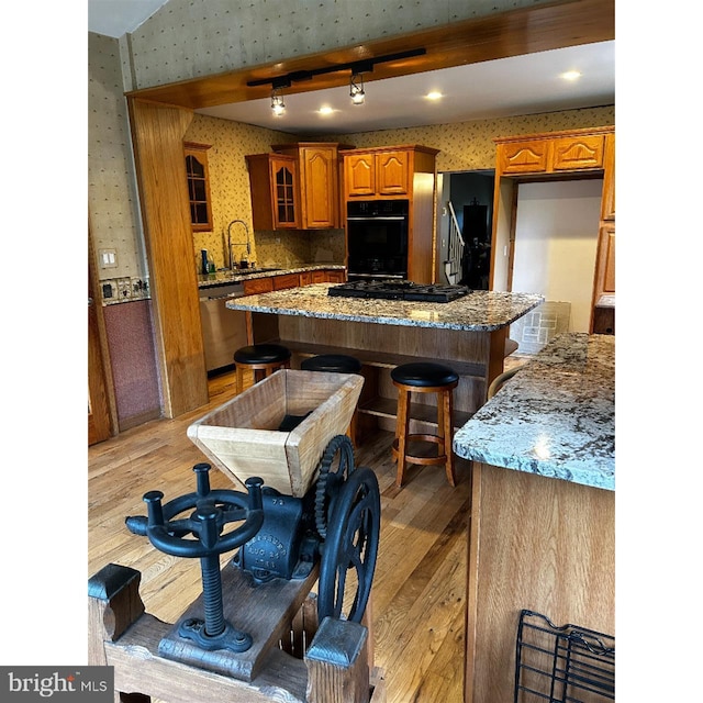 kitchen with wallpapered walls, black appliances, a sink, brown cabinetry, and light wood finished floors