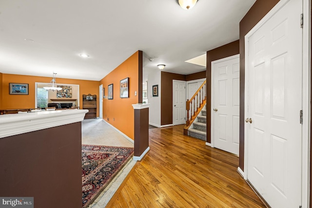 hallway with a chandelier, stairs, light wood-type flooring, and baseboards