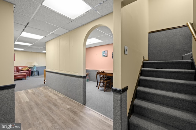 stairway with a drop ceiling, wood finished floors, carpet flooring, and arched walkways