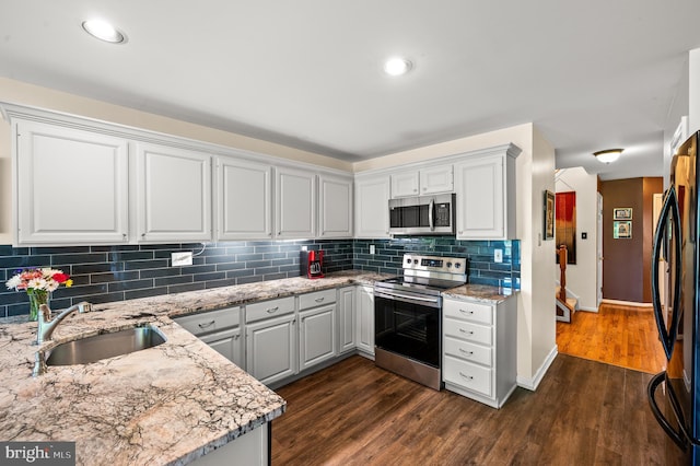 kitchen with stainless steel appliances, a sink, light stone countertops, dark wood-type flooring, and recessed lighting