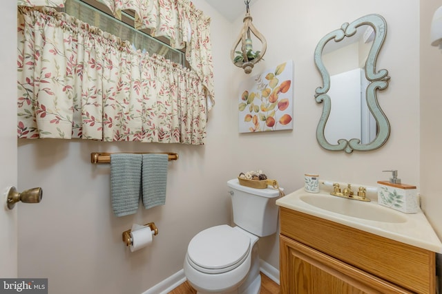 half bathroom featuring toilet, vanity, and baseboards