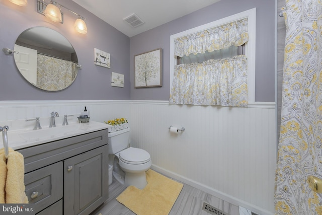 bathroom with toilet, wainscoting, vanity, and wood finished floors