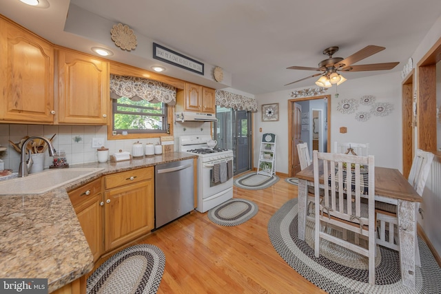 kitchen with stainless steel dishwasher, white range with gas cooktop, a sink, light wood-type flooring, and decorative backsplash