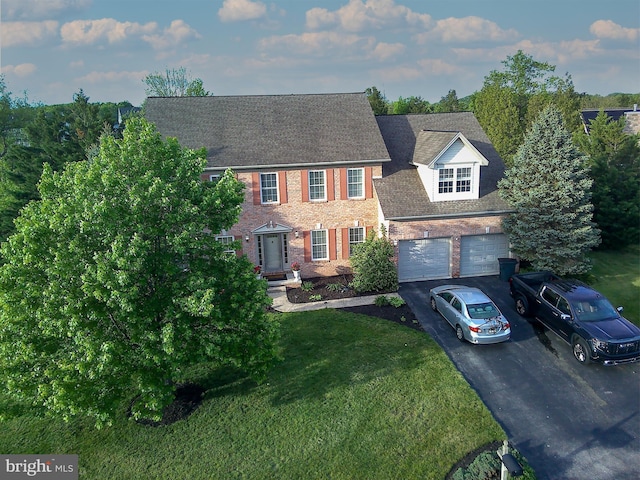 colonial inspired home featuring asphalt driveway, a front lawn, brick siding, an attached garage, and a shingled roof