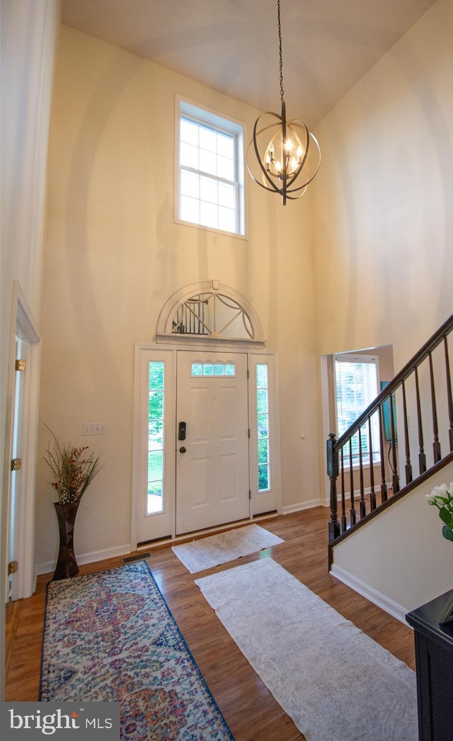 foyer entrance with a chandelier, a high ceiling, stairway, wood finished floors, and baseboards
