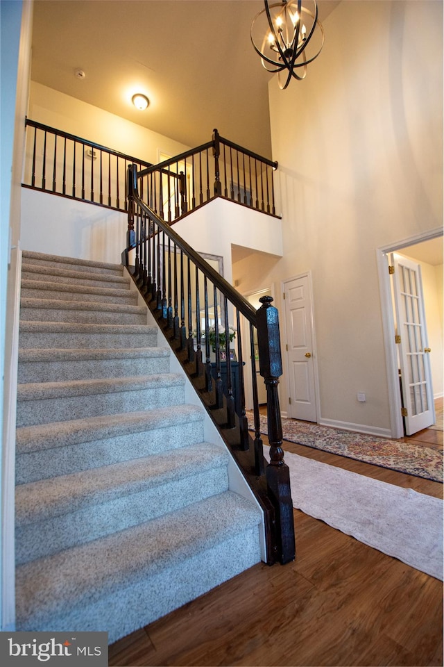 stairs featuring wood finished floors, baseboards, a chandelier, and a towering ceiling