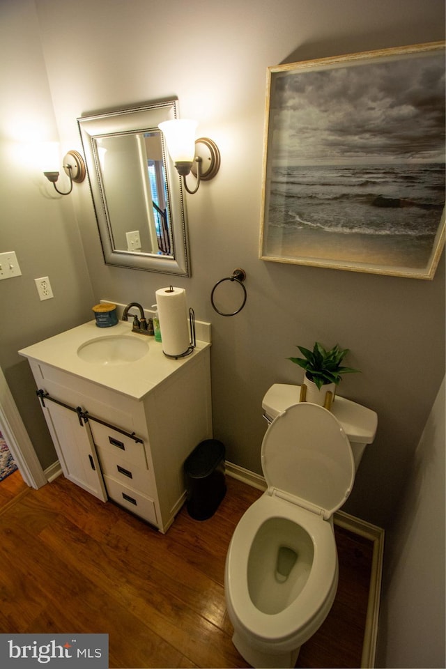 half bath with wood finished floors, vanity, toilet, and baseboards