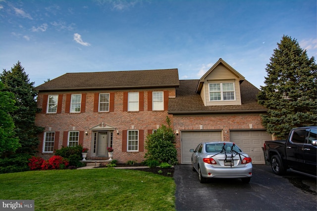 colonial inspired home with asphalt driveway, brick siding, a front yard, an attached garage, and a shingled roof