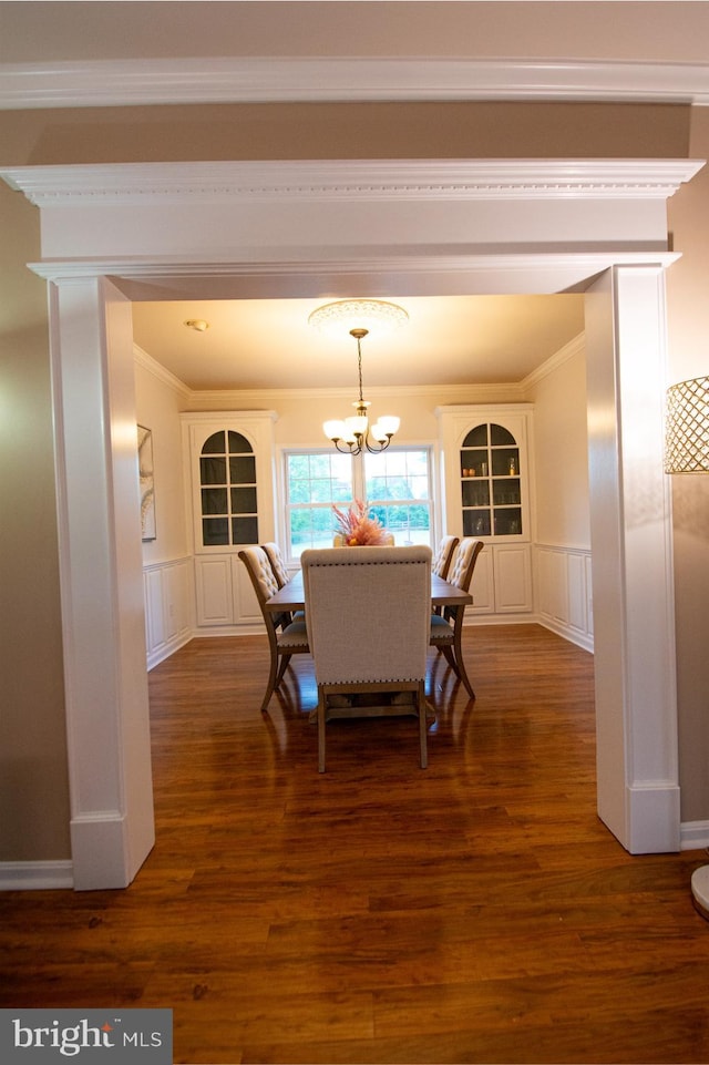 dining space featuring ornamental molding, a decorative wall, dark wood-style flooring, a chandelier, and wainscoting