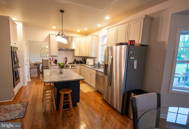 kitchen with appliances with stainless steel finishes, wall chimney range hood, a sink, light wood finished floors, and recessed lighting
