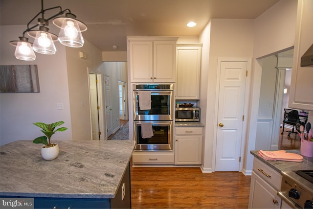 kitchen with stainless steel appliances, wood finished floors, white cabinetry, light stone counters, and a kitchen island