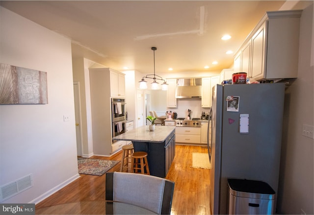 kitchen with stainless steel appliances, a breakfast bar area, a center island, wall chimney exhaust hood, and light wood finished floors